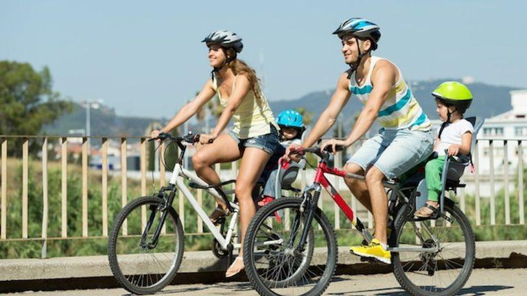 משפחה רוכבת על אופניים יחד בשביל אופניים לצד אגם בלטון